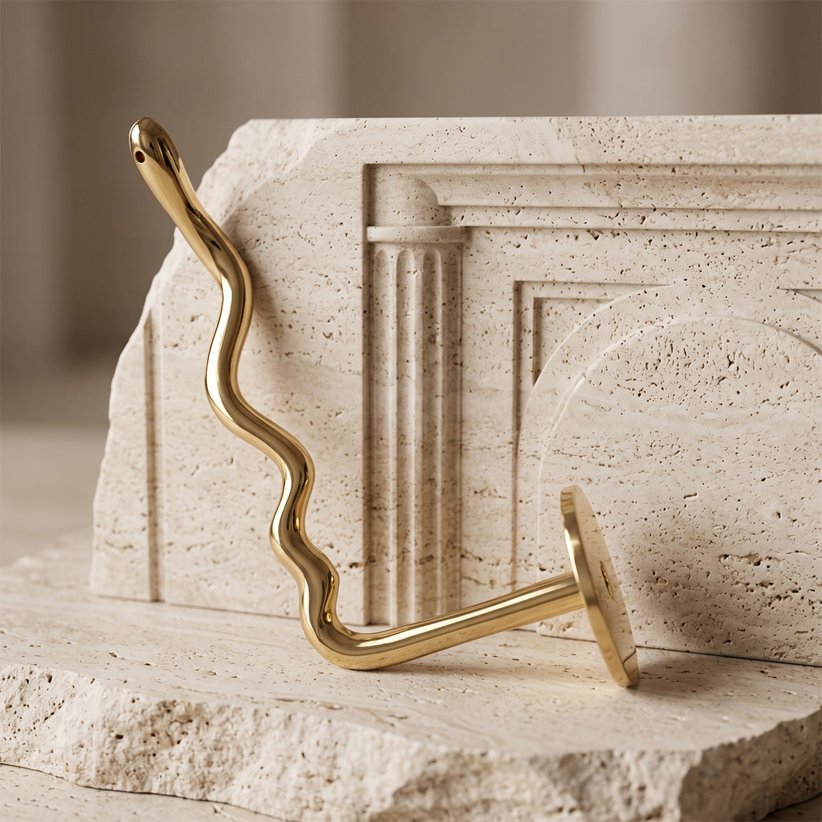 A polished brass wavy toilet paper holder with a round wall mount, shown against a textured beige plaster wall.